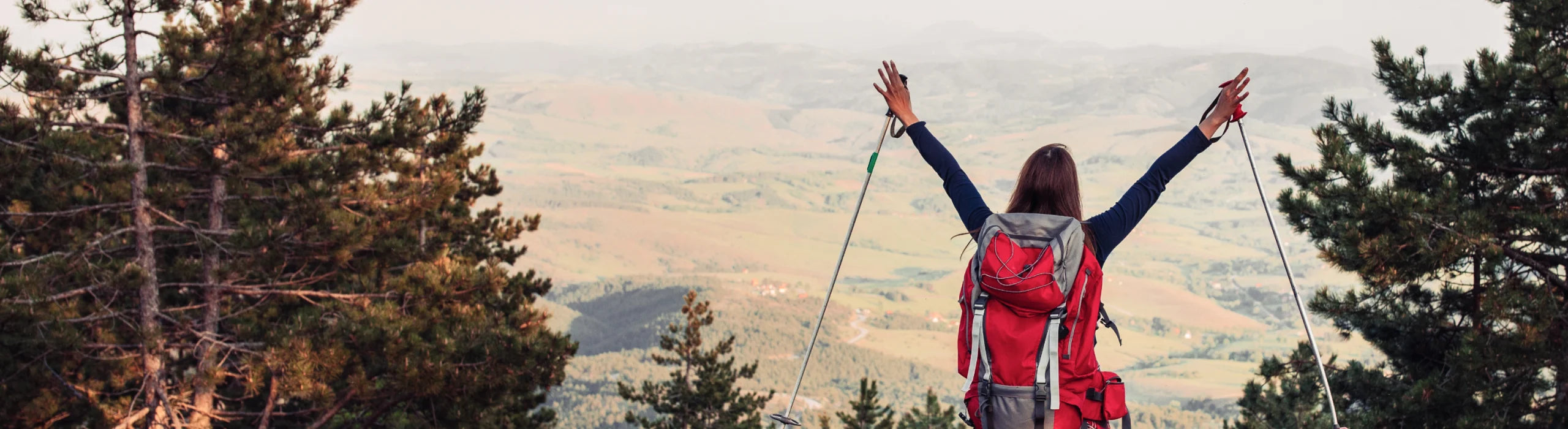 Hiker with arms raised at the top of a mountain looking out at the landscape below.