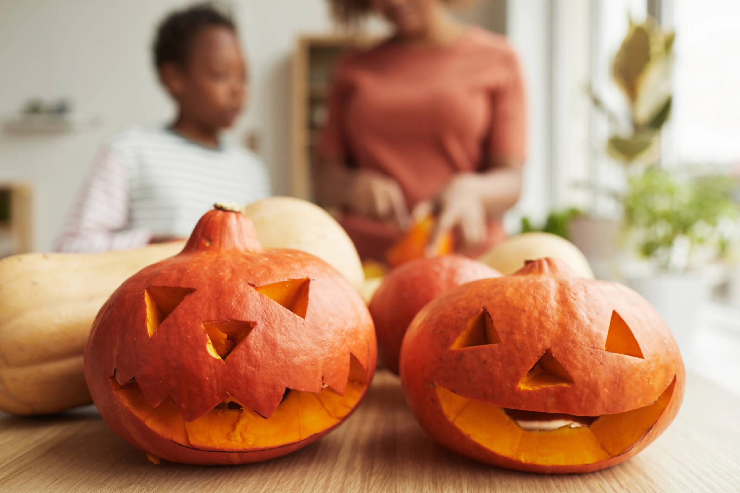 Closeup of two jack-o'-lantern pumpkin carvings with a mother and son in the background.