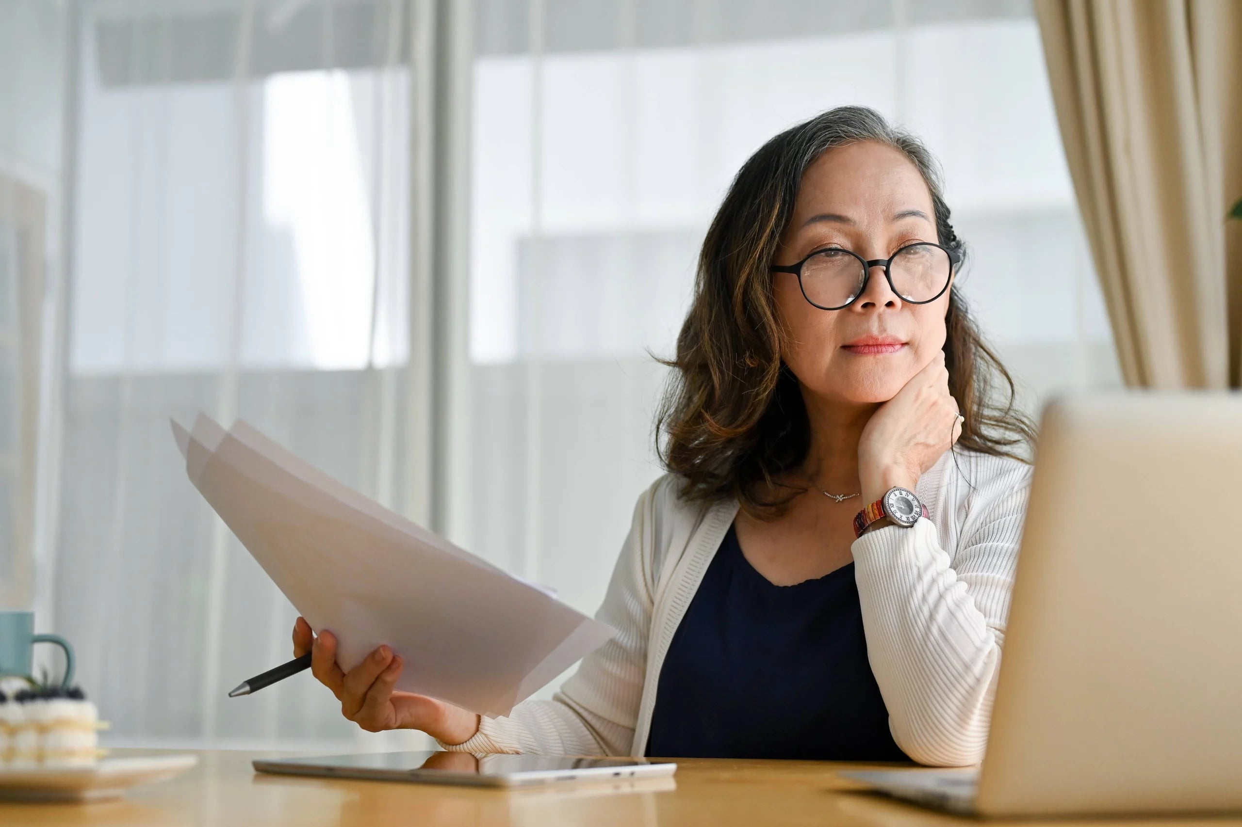 Woman holding paper and looking at a computer screen