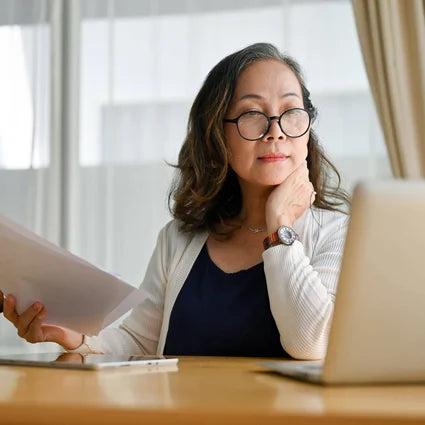 Woman holding paper and looking at a computer screen